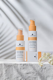 Two skincare bottles with orange caps and white bodies on a light background