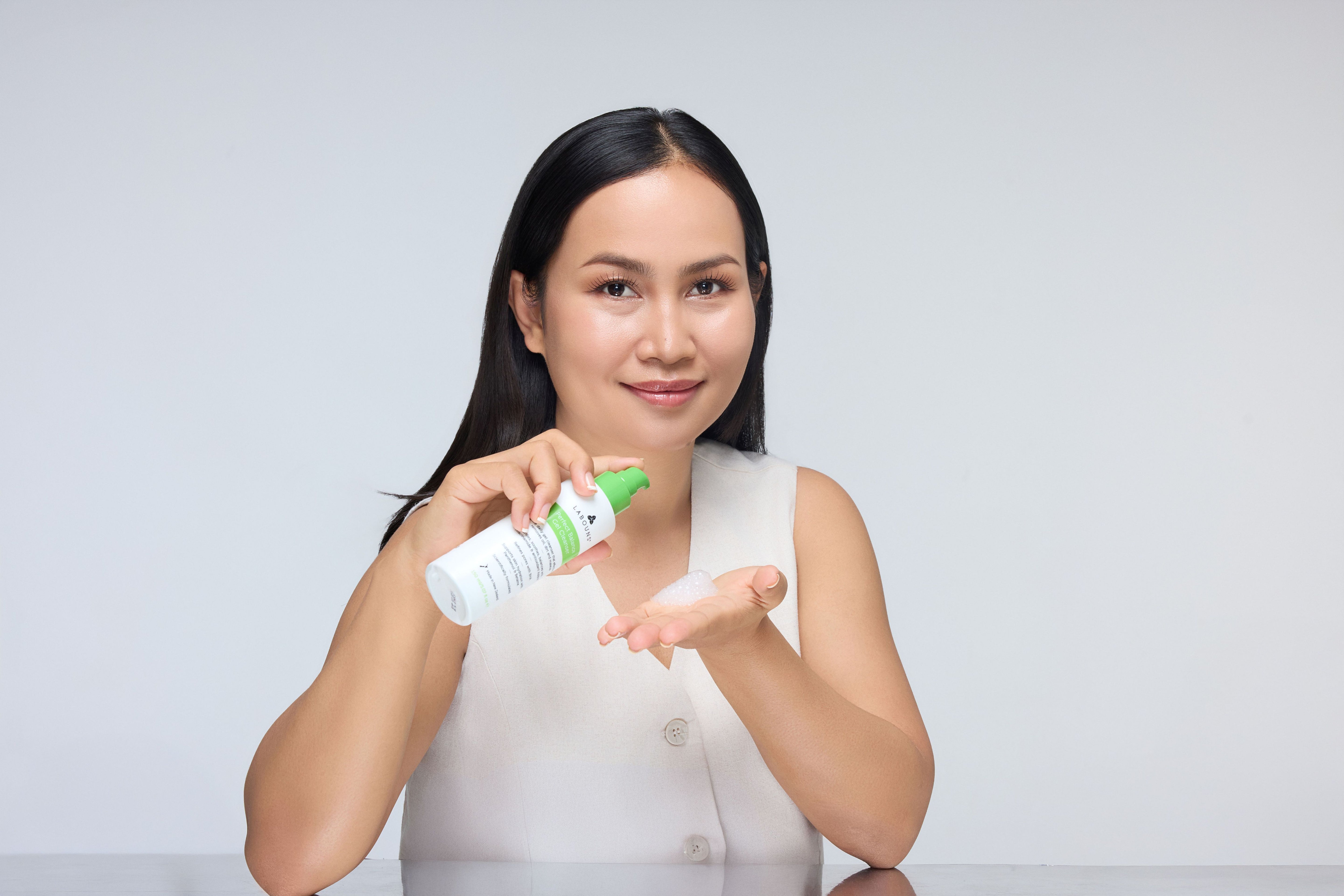 Woman holding a bottle of gel cleanser labeled 'Labouns Perfect Balance Gel Cleanser' against a white background