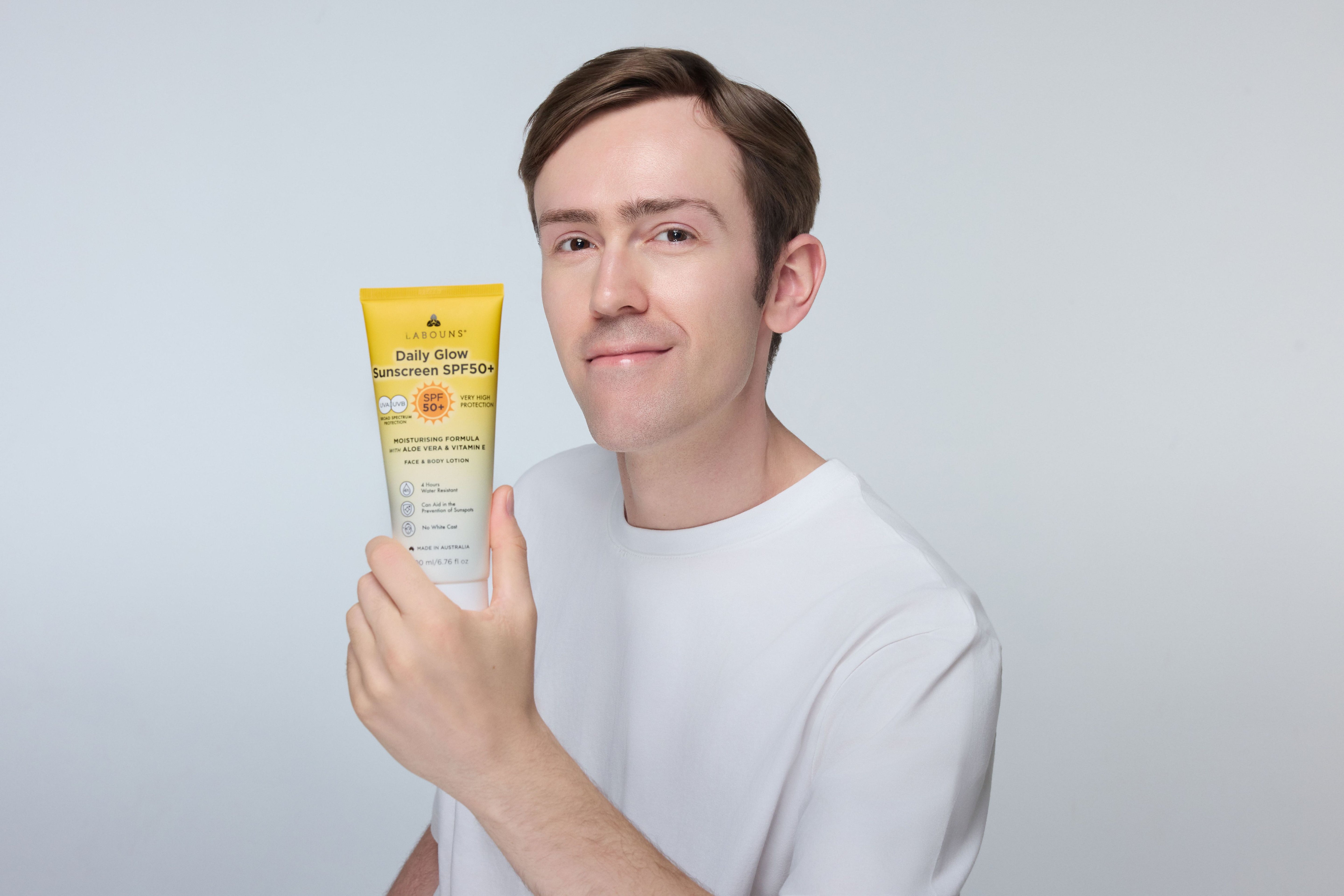 Man holding a tube of 'Labouns Daily Glow SPF50+' sunscreen on a light gray background