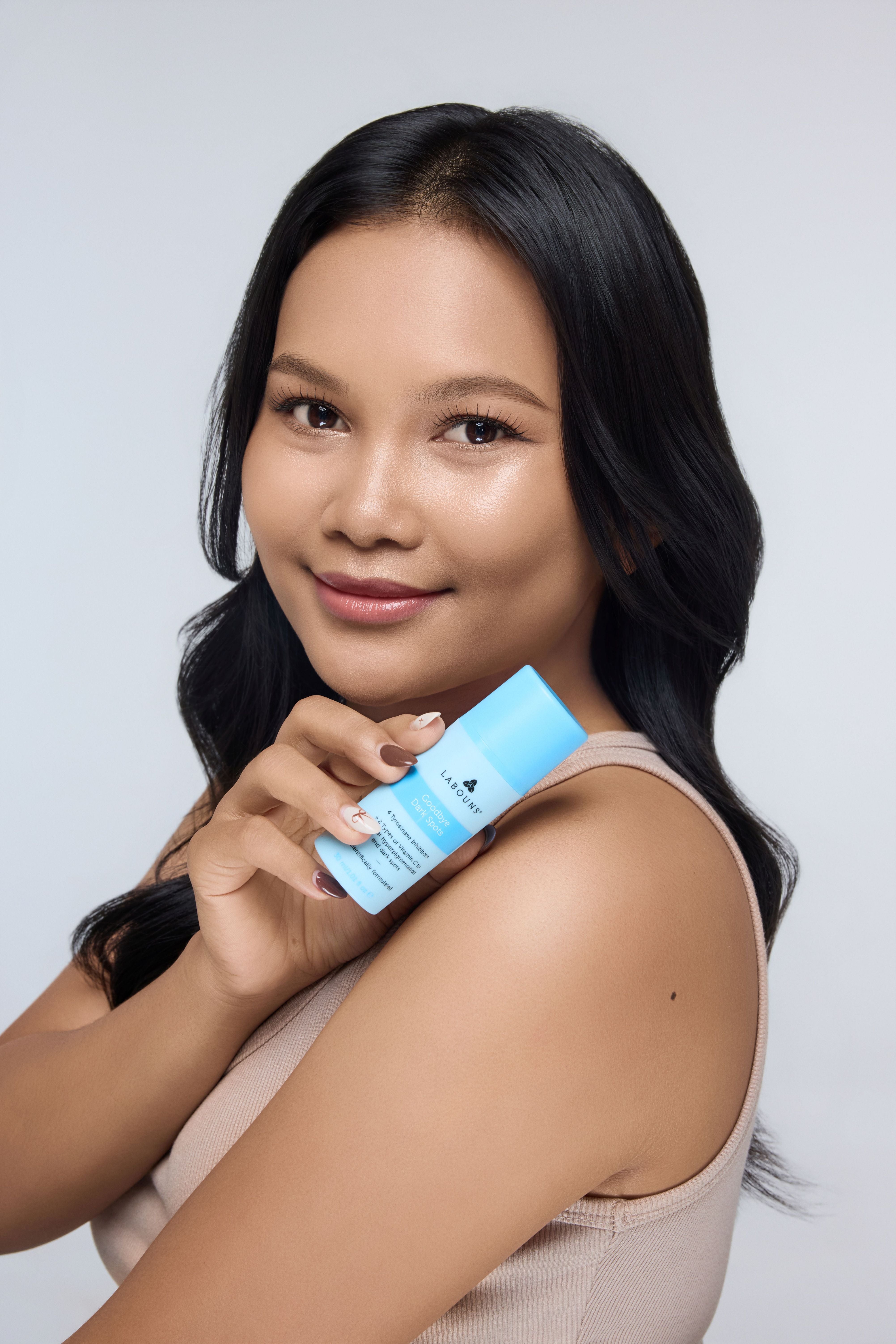 Woman holding a blue skincare product labeled 'Labouns Goodbye Dark Spots' against a light gray background