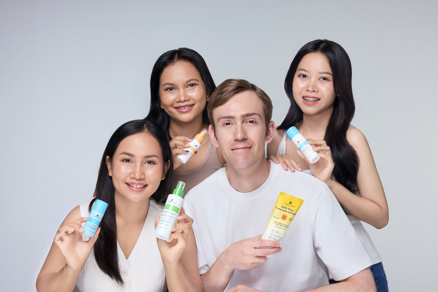 Three women and a man holding Labouns skincare products against a plain background