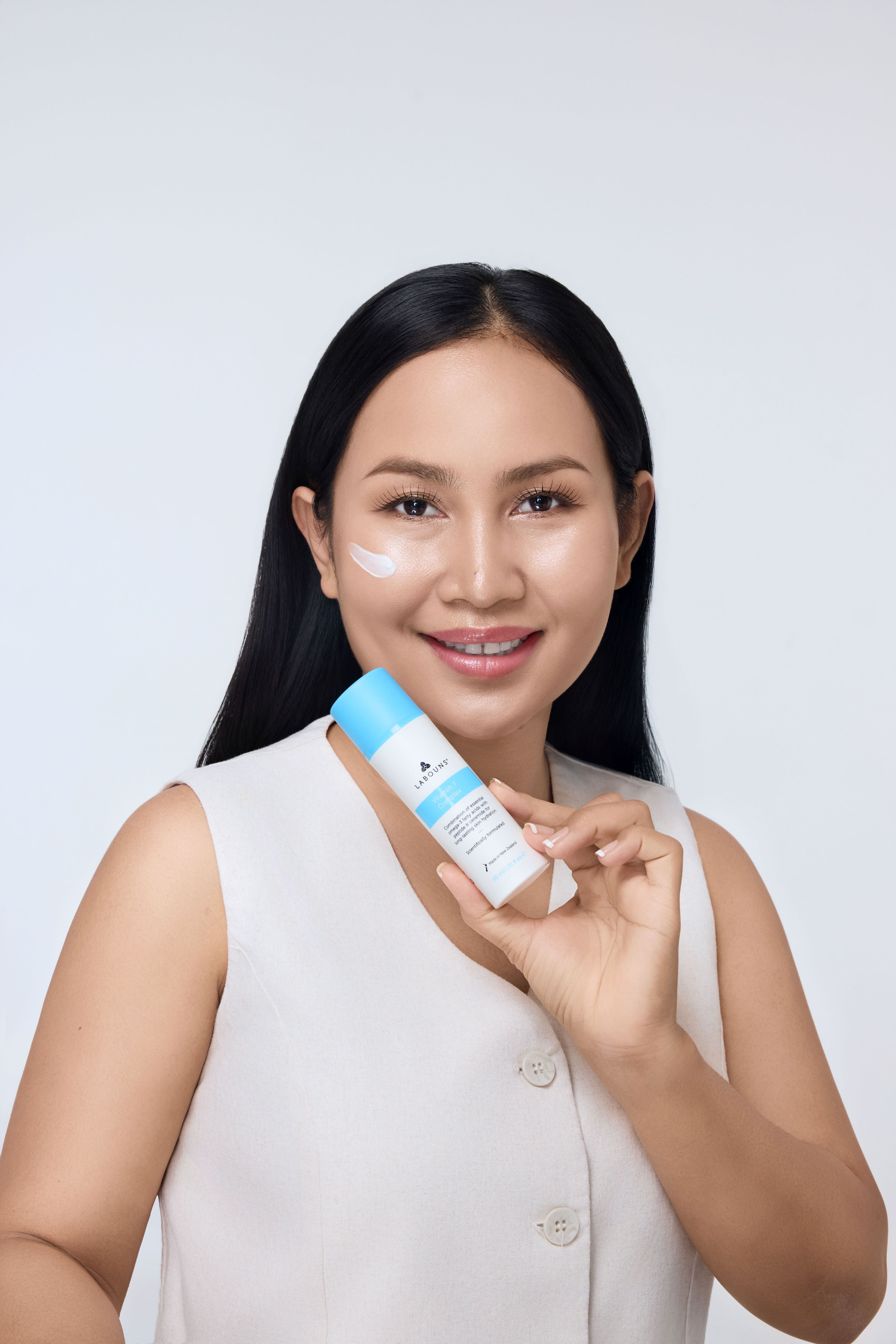 Woman holding a white tube with a blue cap labeled 'Labouns Vitamin F Complex' with a white background